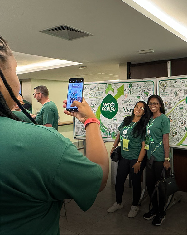 Colaboradores fotografam painel de facilitação visual criado ao vivo na Convenção de Vendas 2026 da Verde Campo, com mapa estratégico ilustrado ao fundo.
