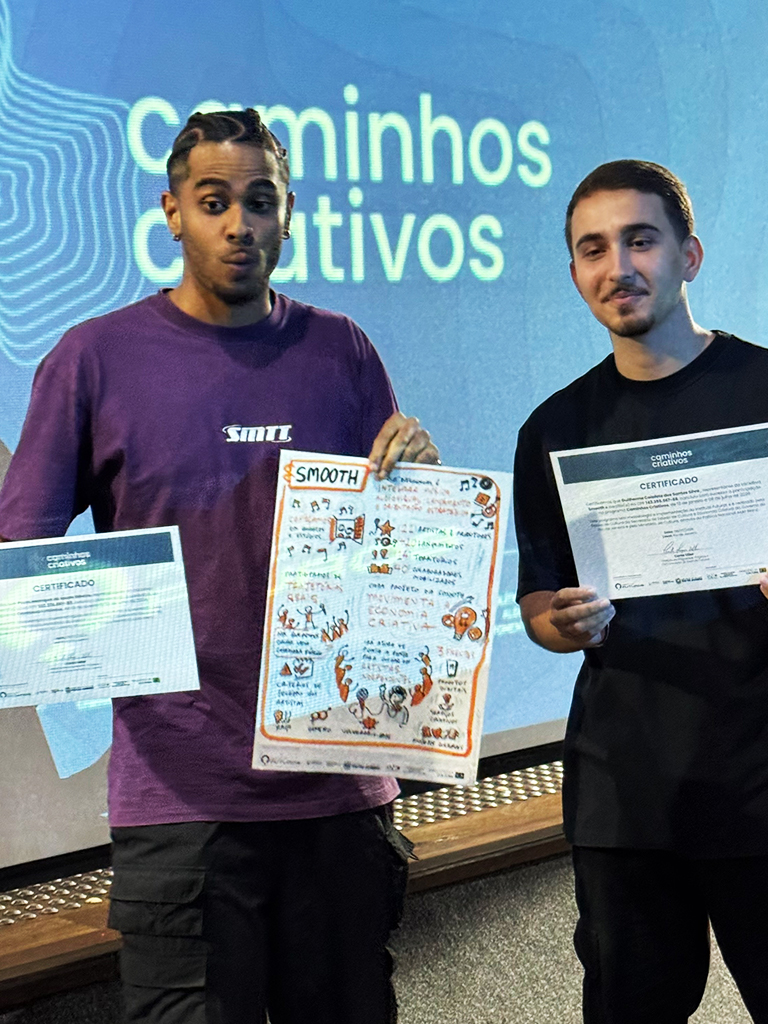 Dois fundadores da produtora cultural SMOOTH seguram os seus certificados e a prancha de facilitação gráfica do seu pitch no evento Caminhos Criativos.
