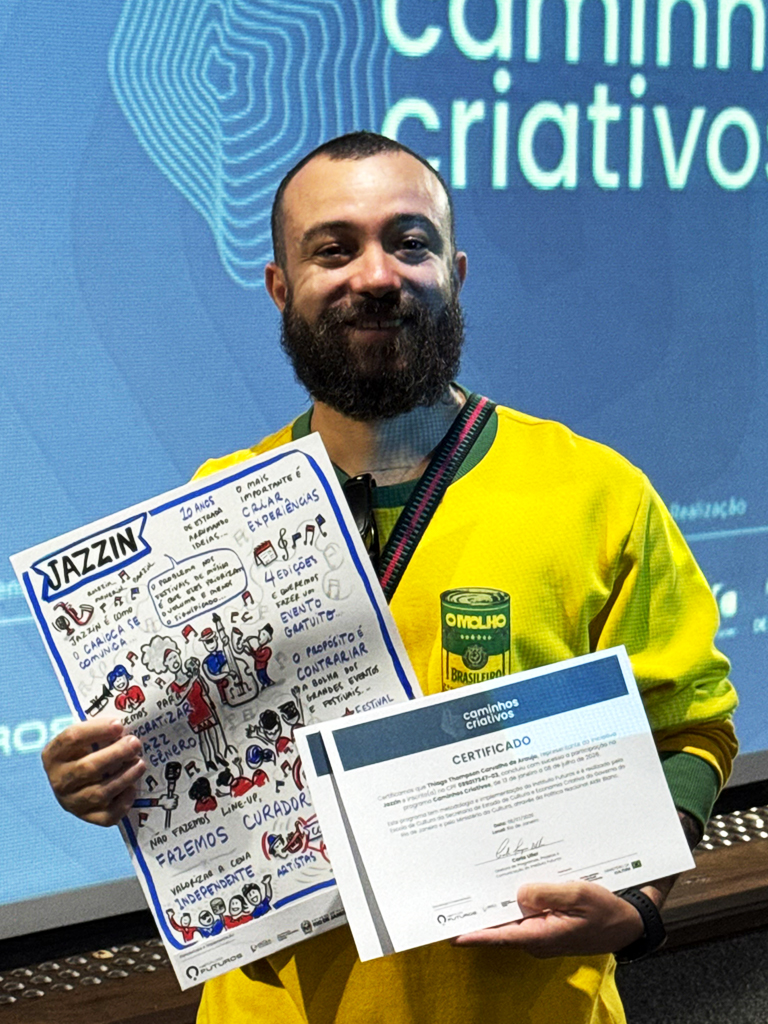 Empreendedor a segurar a prancha de facilitação gráfica do Festival Jazzin e o certificado do programa Caminhos Criativos.
