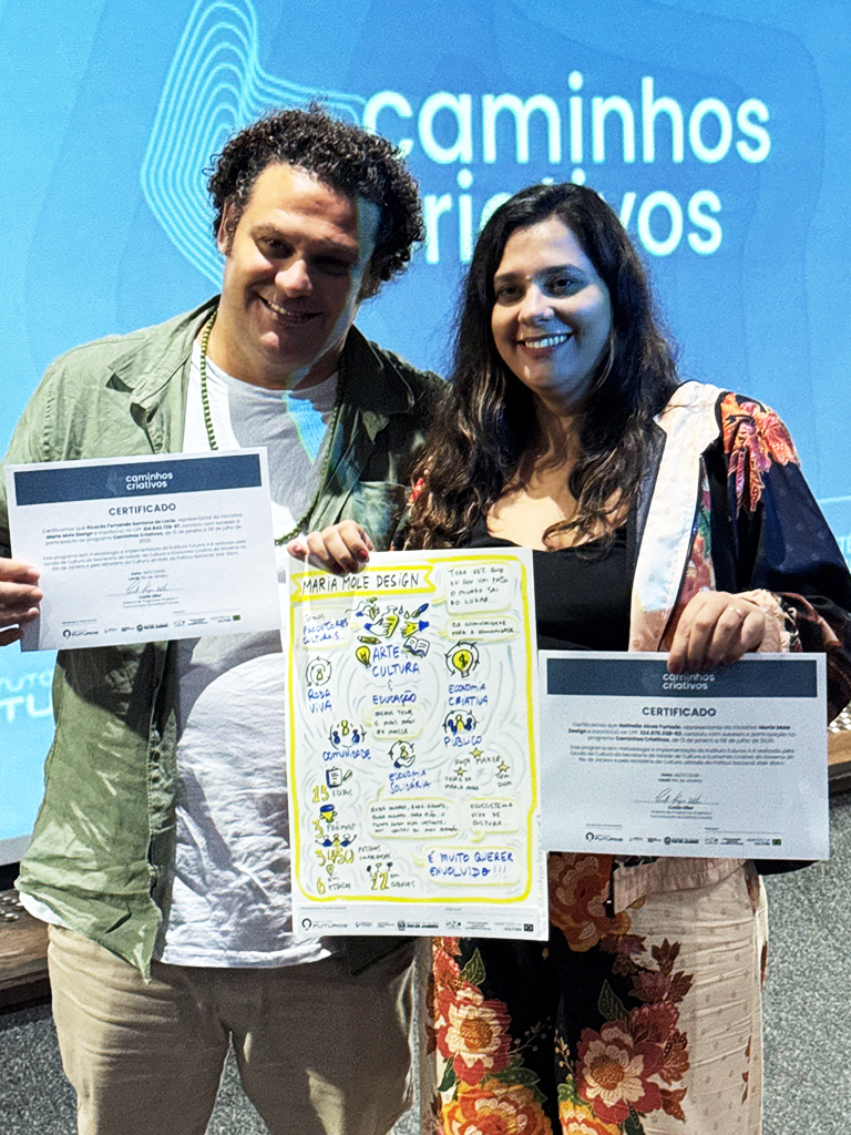 Dois empreendedores a sorrir enquanto seguram juntos a prancha ilustrada do projeto Maria Mole Design e os seus certificados.